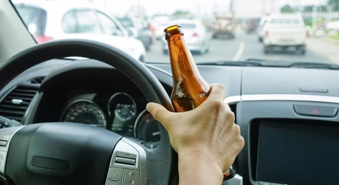 Человек с бутылкой пиво управляет автомобилем